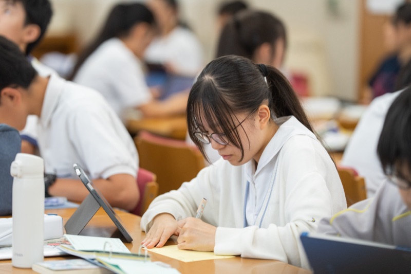 図書館で調べ物をしながら書き込む生徒